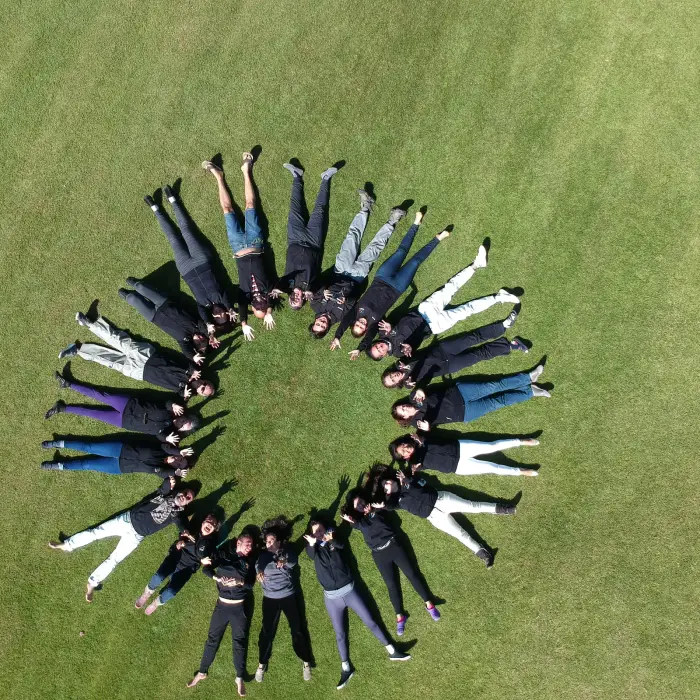 Grupo de personas acostadas en disposición radial sobre el pasto, vista en picada, foto de dron