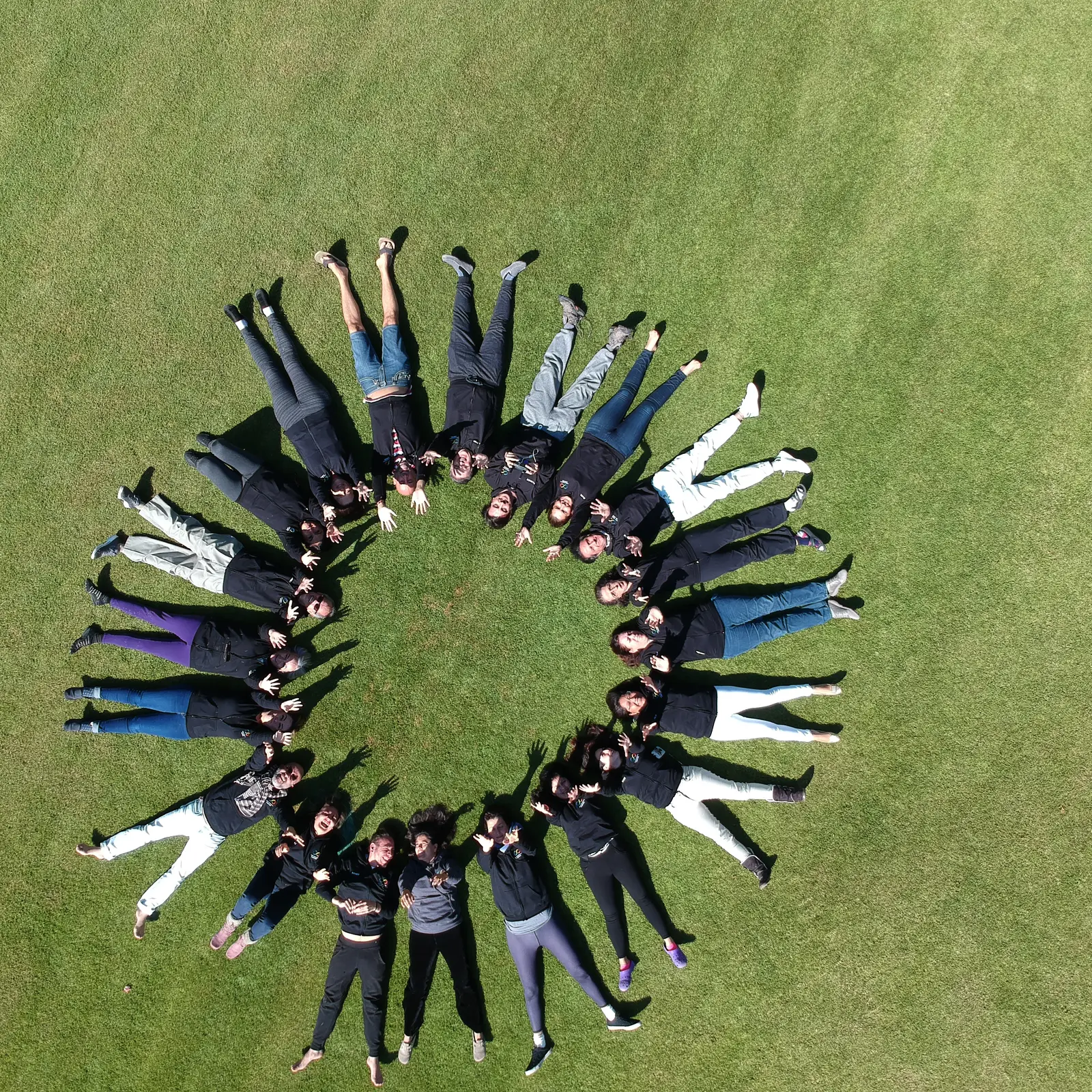 Grupo de personas acostadas en disposición radial sobre el pasto, vista en picada, foto de dron